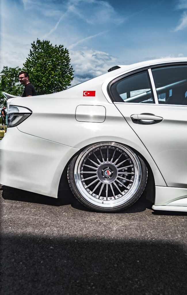 A white car with custom wheels and a Turkish flag decal on a sunny day.