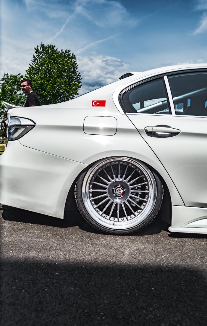 A white car with custom wheels and a Turkish flag decal on a sunny day.